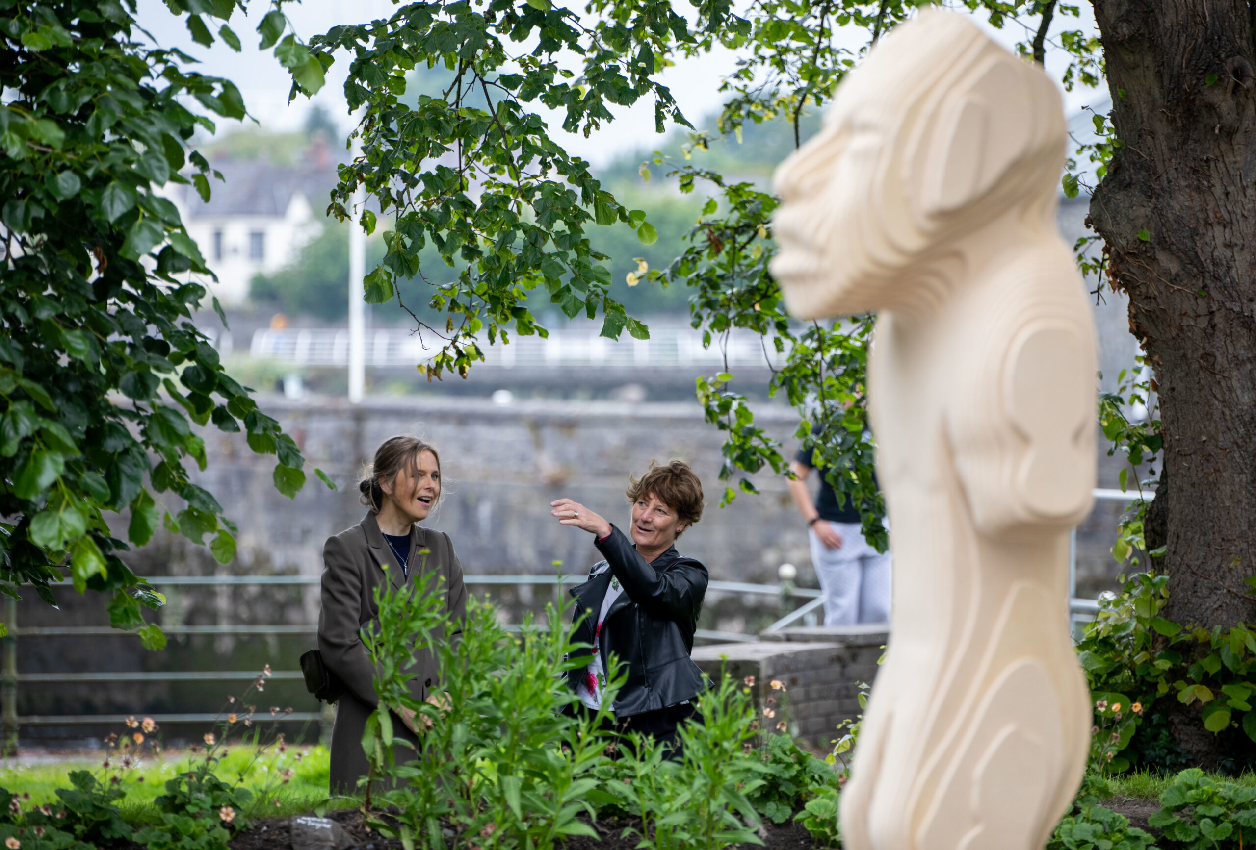 Two people standing the museum garden talking by the Olmec man.