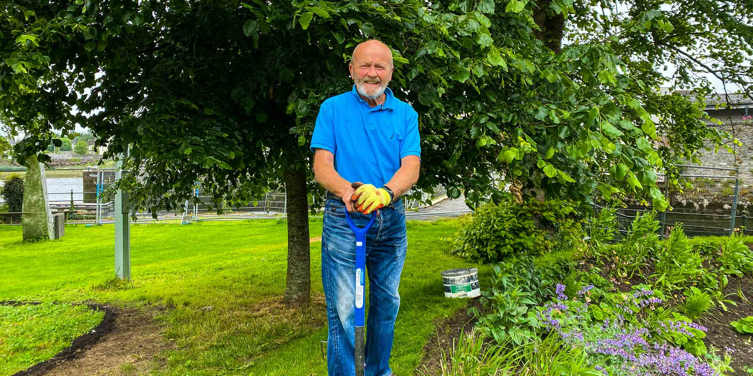 A volunteer standing in the garden, posed with a shoved in his hand.