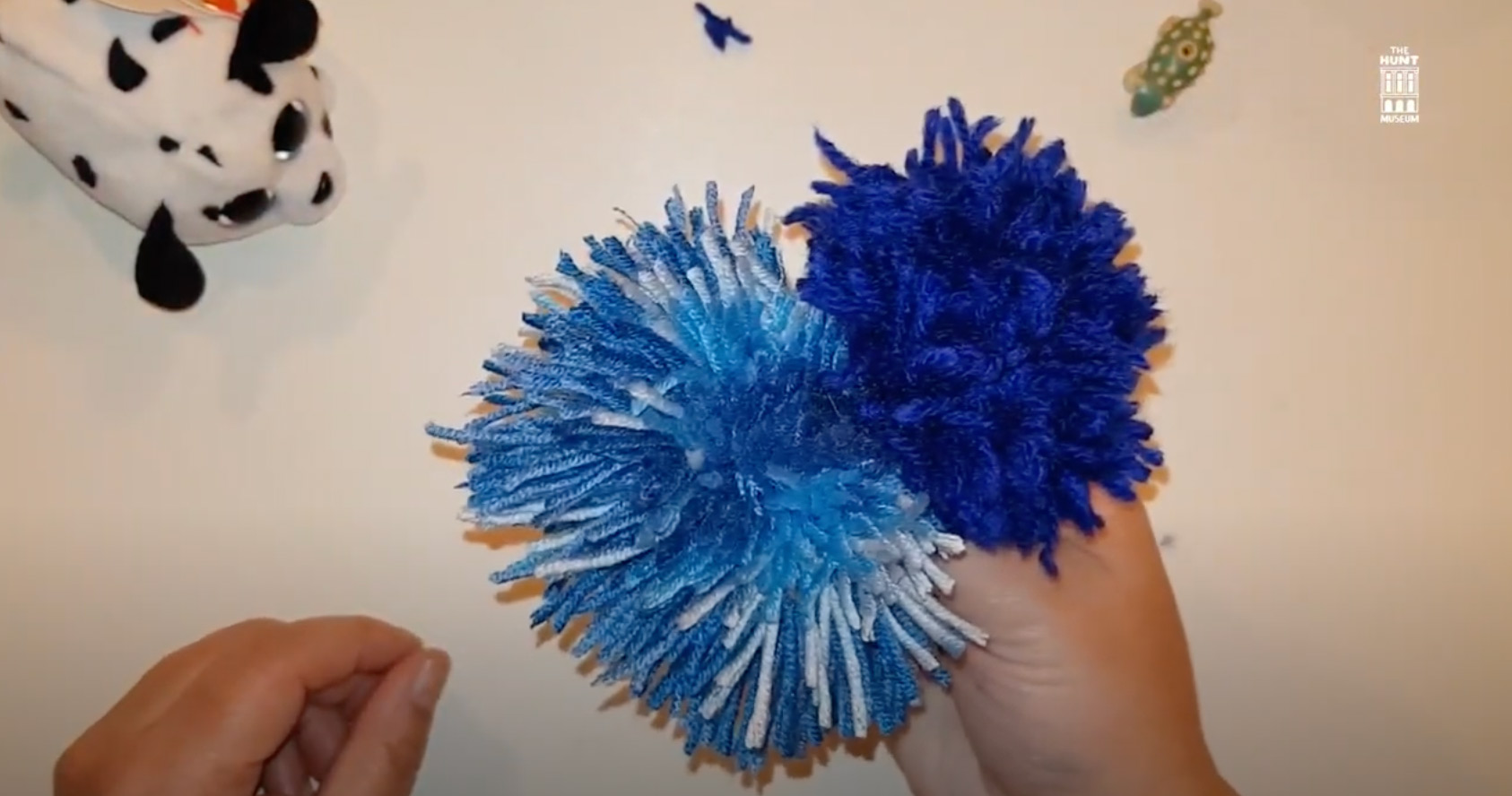 Pompom. Image of hands holding two DIY blue pom-poms.