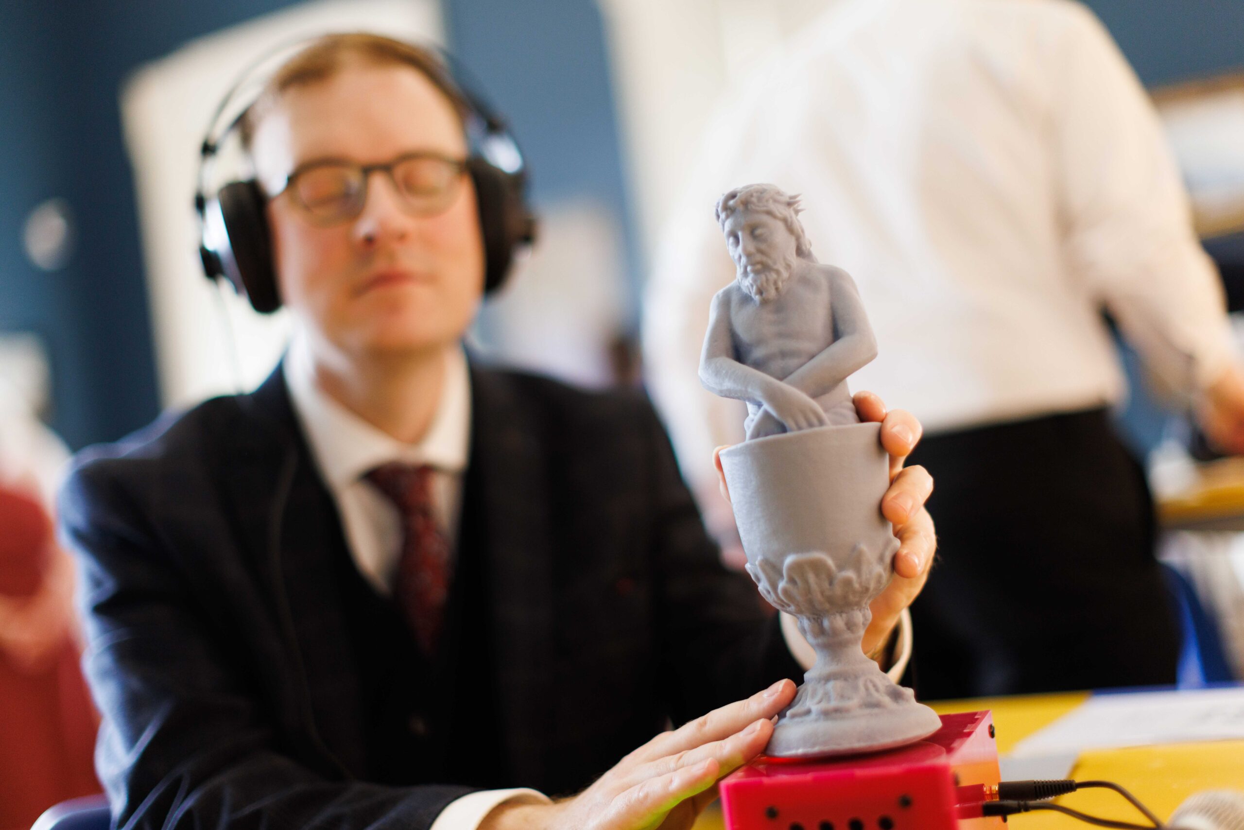 A man with visual impairment holds a 3D model of an object, while listening to an audio piece through headphones.