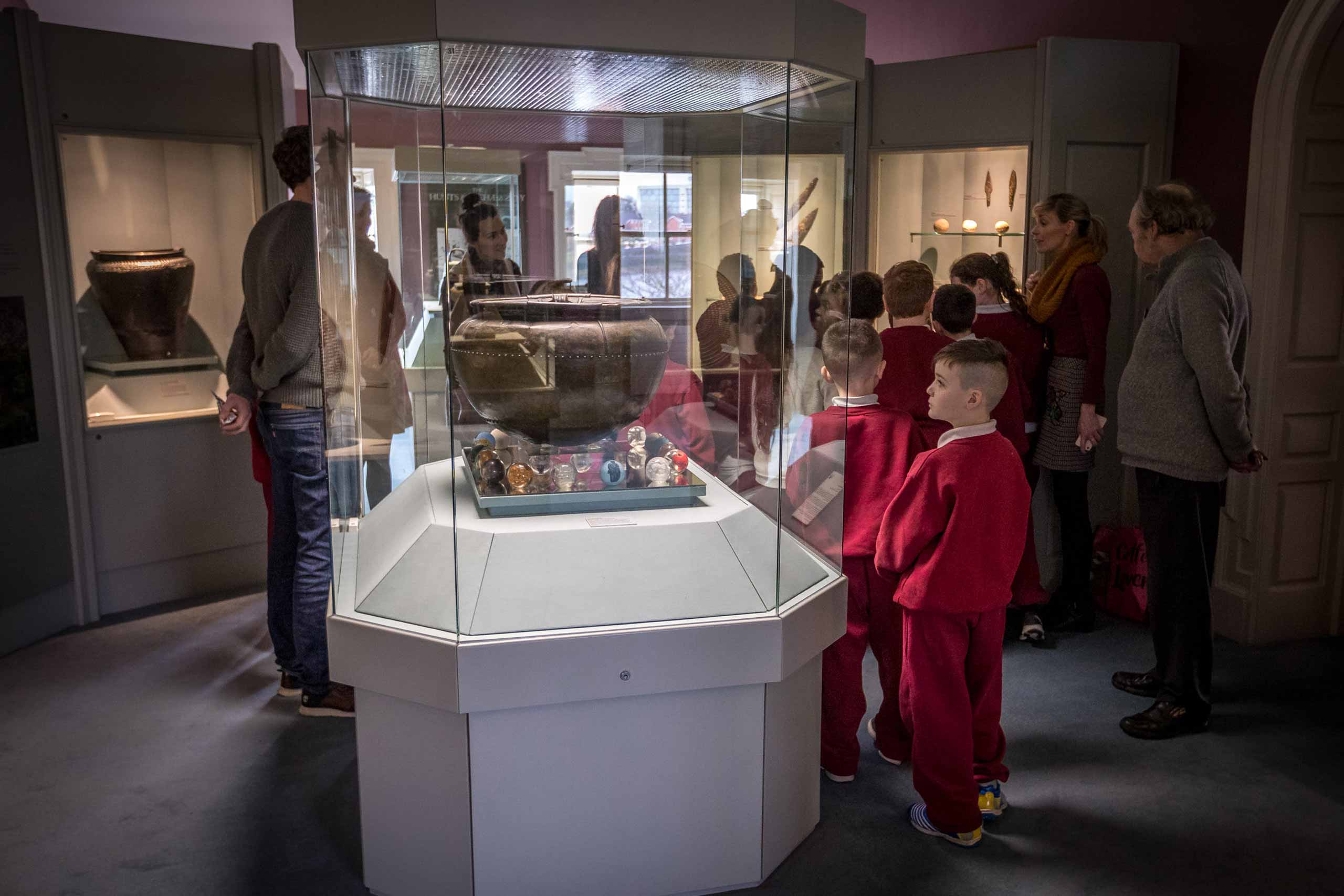 A group of schoolchildren are being shown around a room in the museum with glass display cases containing artefacts Primary Schools