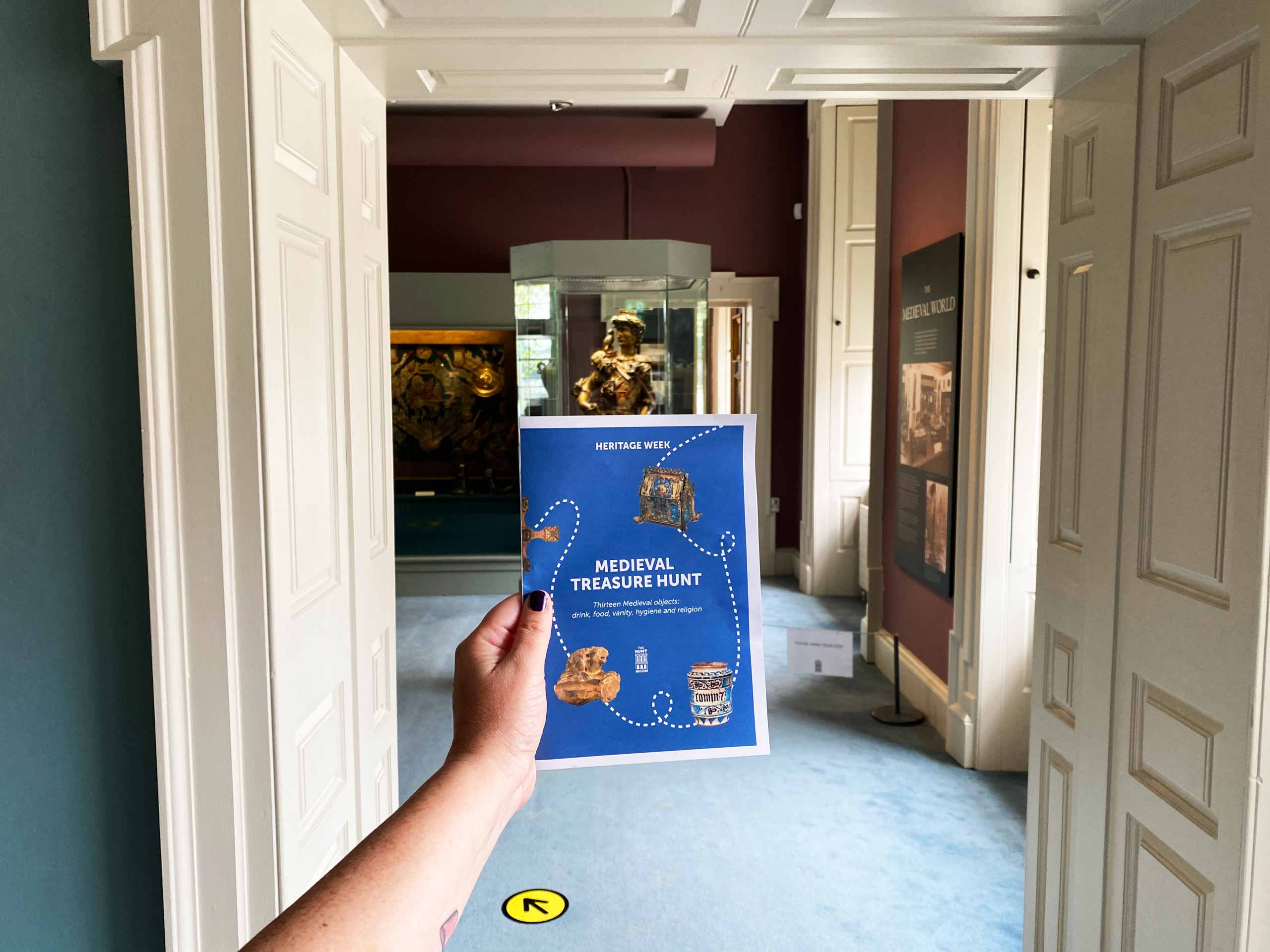 A hand holding a Hunt Museum trail guide booklet with Apollo, God of the Arts, statue in the background.
